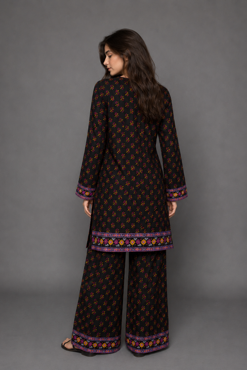 Woman wearing a black patterned outfit with wide-leg pants against a gray background
