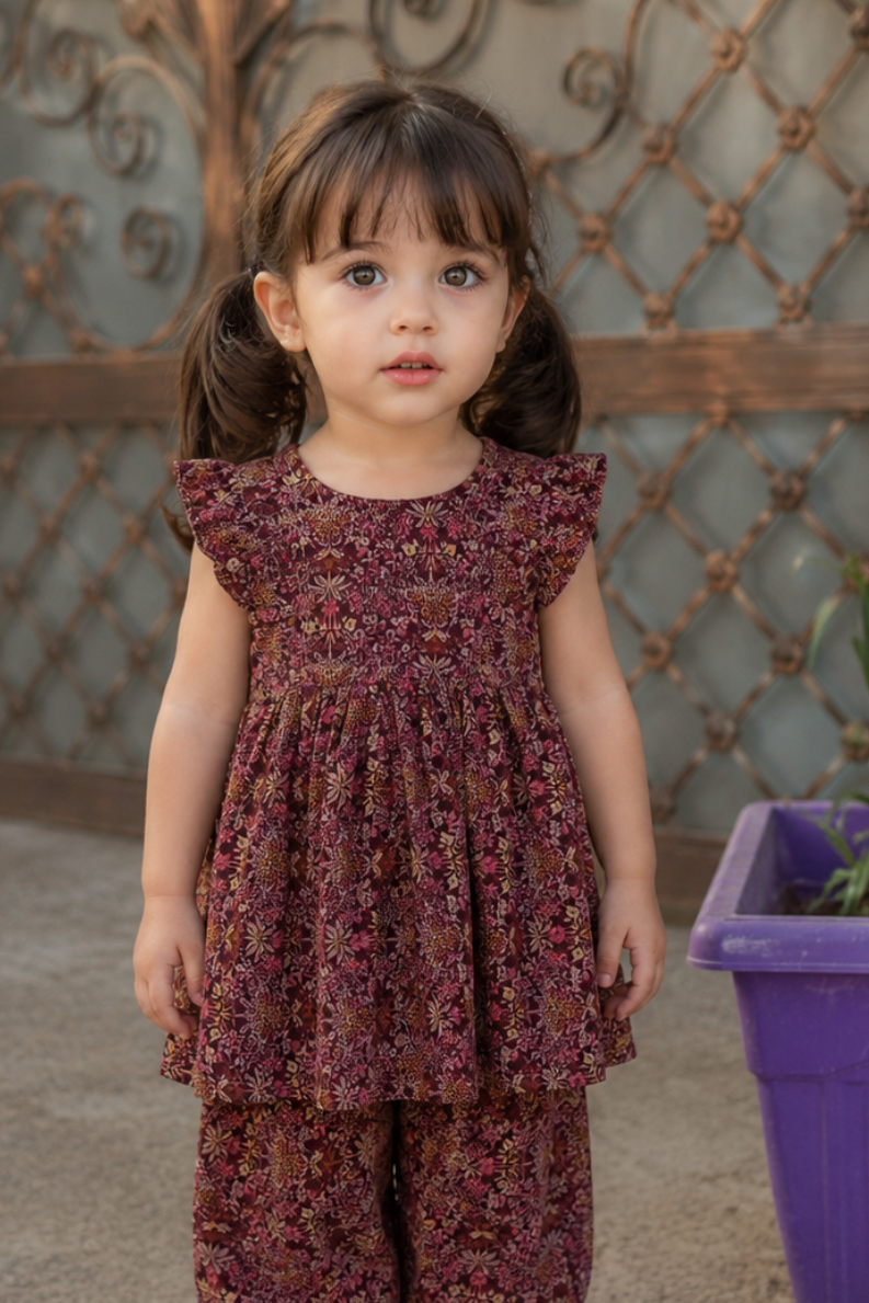 Young girl in a floral dress standing in front of an ornate metal gate.