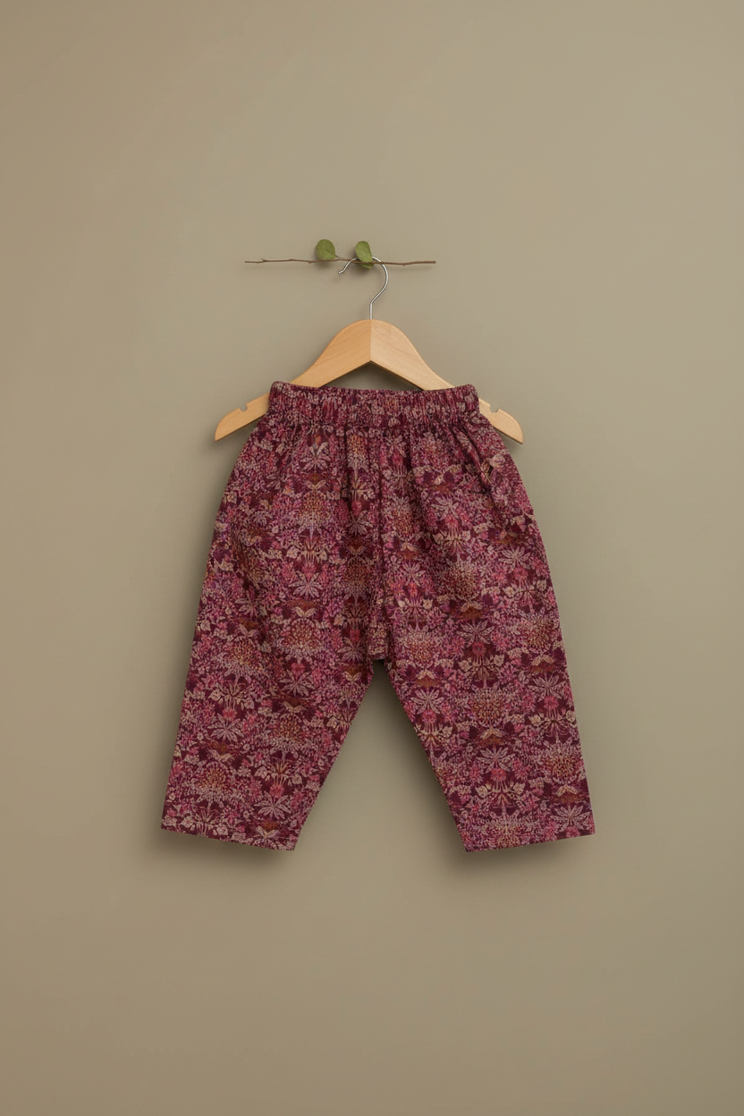 Floral-patterned pants on a wooden hanger against a beige wall