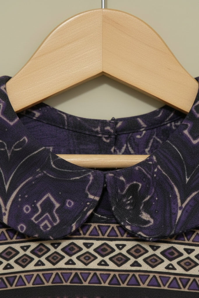 Purple patterned collar on a wooden hanger against a neutral background