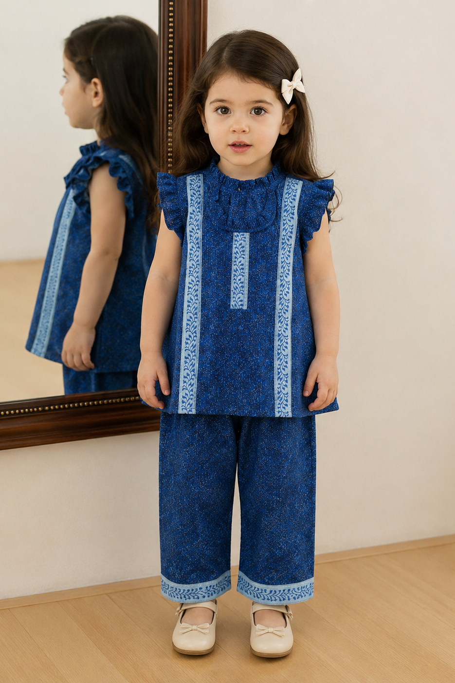Young girl in a blue outfit standing in front of a mirror.