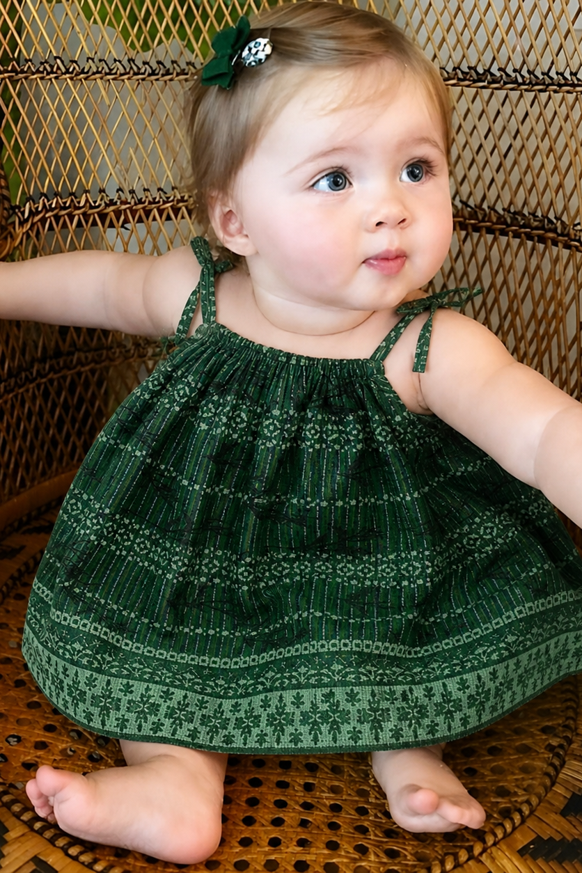 Baby in a green dress sitting on a wicker chair