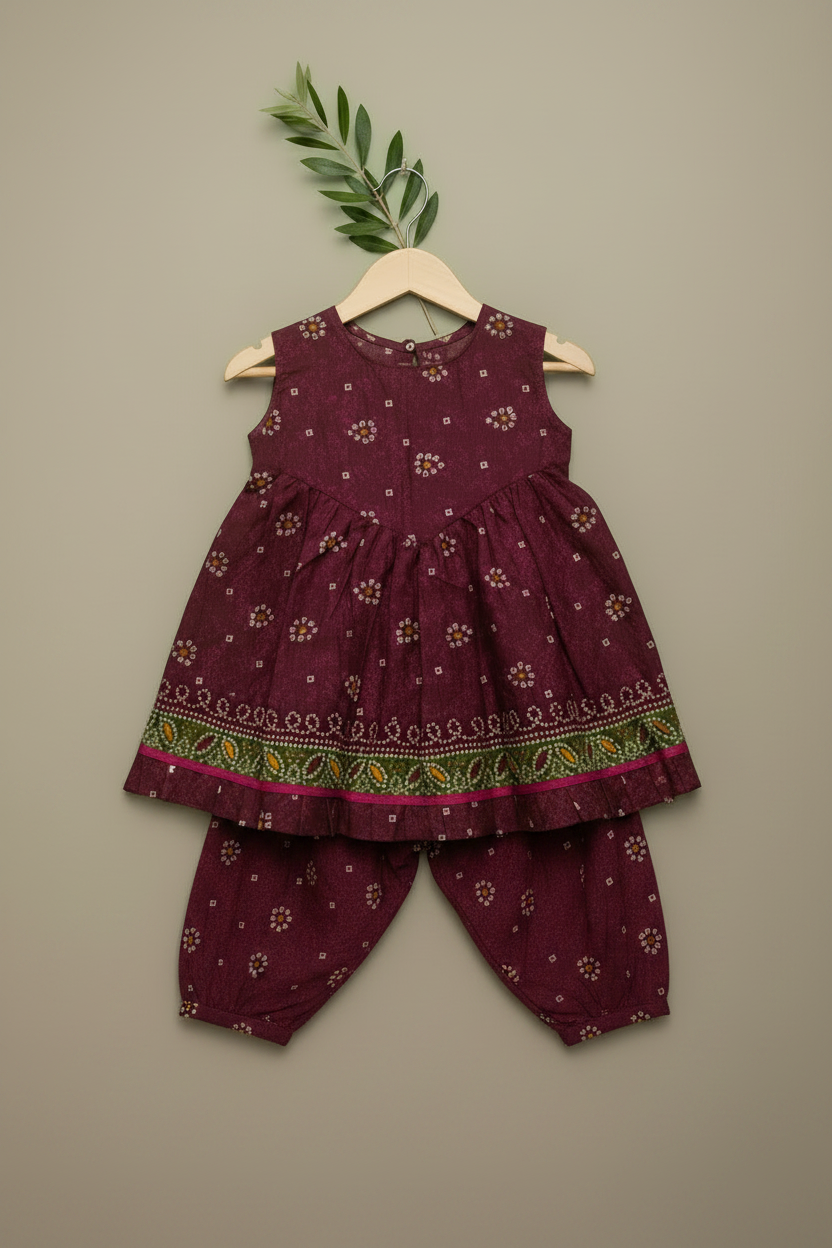 Children's outfit with a maroon dress and pants on a hanger against a beige background.