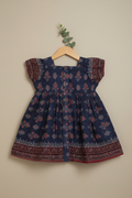 Blue dress with floral pattern on a wooden hanger against a beige wall.