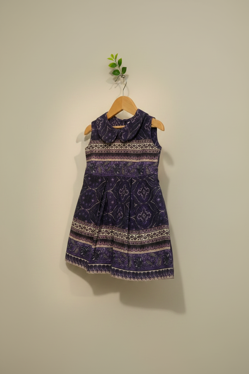 Purple patterned dress on a hanger against a plain wall