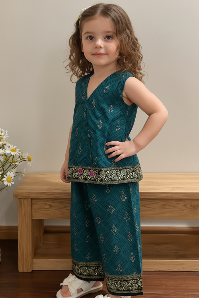 Young girl in a teal traditional outfit standing in a room with a wooden bench and flowers.